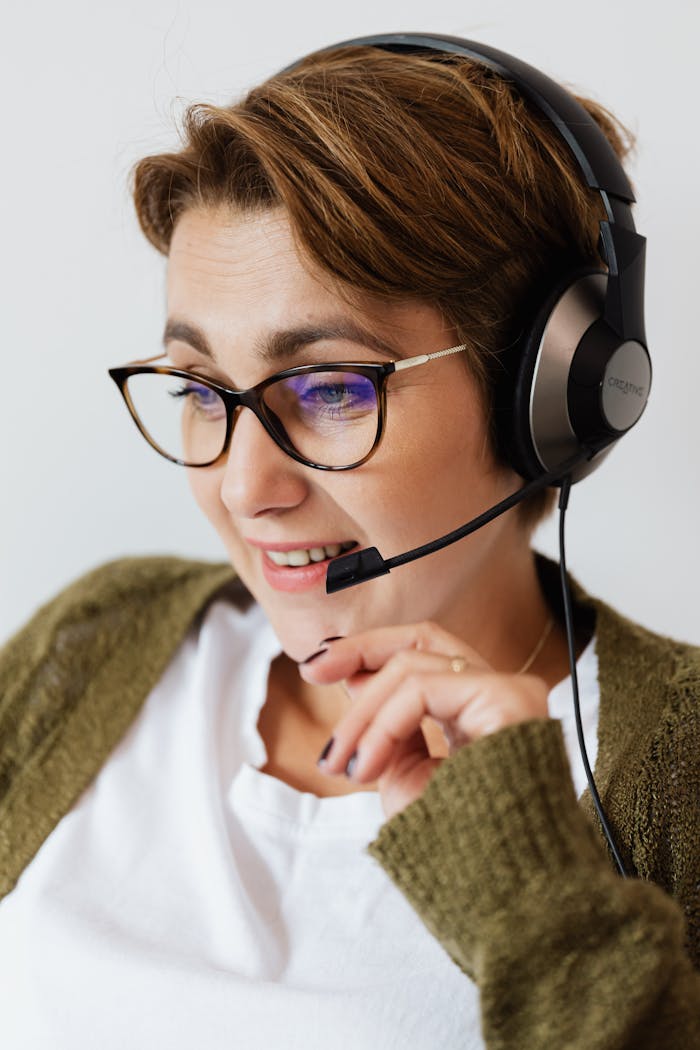 Portrait of a young woman in eyeglasses wearing headphones, smiling and looking down.