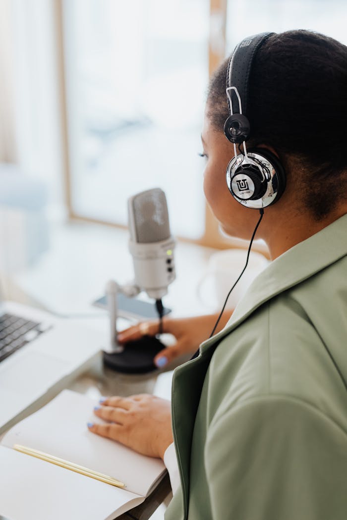 Back view of a woman recording a podcast indoors using a microphone and headphones.